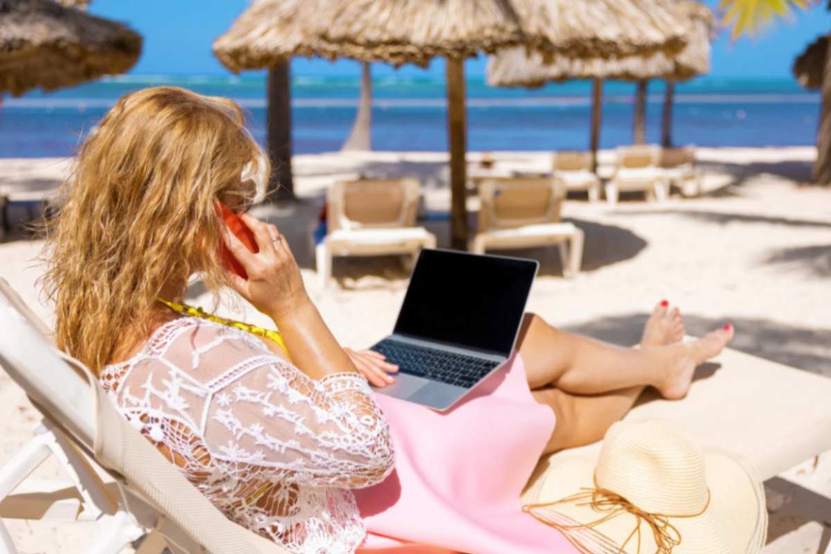 donna con cellulare e computer che lavora dalla spiaggia