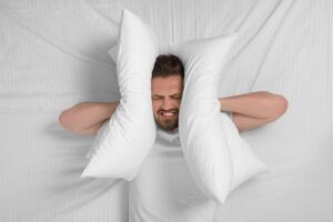 Uomo sul letto che si tappa le orecchie con il cuscino