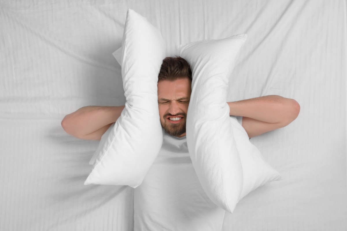 Uomo sul letto che si tappa le orecchie con il cuscino