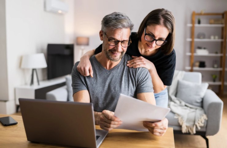 uomo e donna che sorridono mentre leggono dei fogli davanti ad un computer